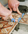 Hands using Tile Leveling System Kit with 1000 Spacers One Sixteenth Inch Pro Grade Horseshoe U Shaped Clips on patterned tiles