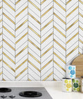Herringbone Peel And Stick Backsplash Tiles With Self Adhesive Marble Look For Kitchen And Bath 10 Sheets Covering About 10 Sq Ft Waterproof Heat Resistant Stain Resistant Anti Scratch White Mixed Gold Metal installed behind a stove in a kitchen.