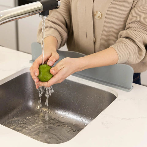 Silicone Sink Splash Guard with Non Slip Suction Base for kitchen and bathroom, gray, shown behind sink catching splashes.