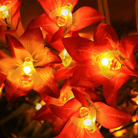 Solar Honey Bee String Lights With 20 Led Outdoor Waterproof Decor For Garden Patio And Xmas, glowing warm honey bee LEDs among red flowers.