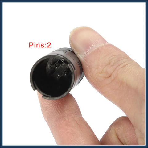 Close-up of a two-pin car brake pad wear sensor, black plastic, held between fingers