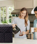 Waterproof Coffee Maker Cover For Keurig Single Serve Brewers in black, protecting a coffee maker on a kitchen counter, diamond-quilted.