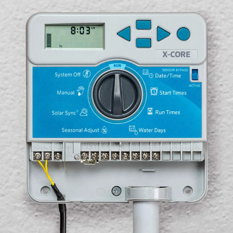 Close-up of X Core XC400i Indoor Sprinkler Timer Four Zone Irrigation Controller with display and control buttons, mounted indoors.