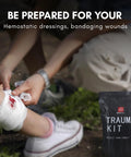 Front view of a black compact IFAK trauma kit pouch labeled TRAUMA KIT beside a person bandaging a leg wound.