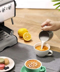 Pro Grade Commercial Semi Automatic Espresso Machine In Stainless Steel With High Pressure Steam Milk Frother Wand 20 Bar Extraction 110-240V For Busy Cafes next to coffee preparation scene with frothed milk being poured into espresso.