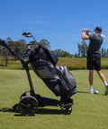 Crush Your Round With This Hella Reliable Electric Golf Push Cart featuring a black golf bag, remote control, on the course.
