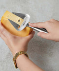 Stainless Steel Cheese Slicer Copenhagen Multifunctional Kitchen Tool used on hard cheese block, handheld with nonstick blade.