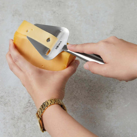 Stainless Steel Cheese Slicer Copenhagen Multifunctional Kitchen Tool used on hard cheese block, handheld with nonstick blade.