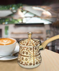 Stainless Steel Turkish Coffee Pot With Long Wooden Handle, Brown Pattern, Multipurpose Kitchen Accessory beside a coffee cup