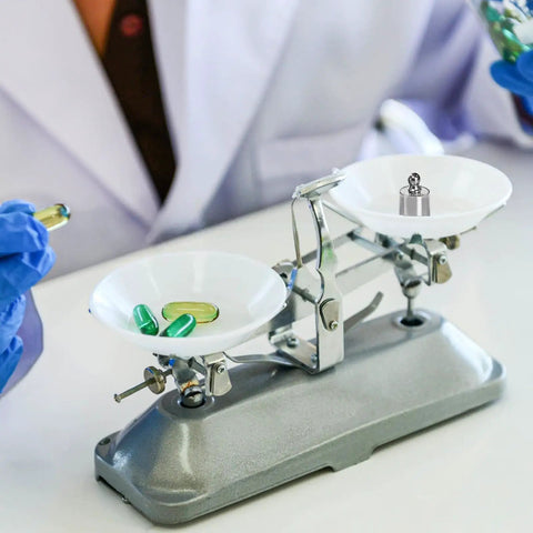 Lab balance scale with pills and a weight from Eight Piece 1000 Gram Total Calibration Weight Set With Tweezers For Digital Scales
