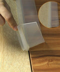 Two Pack 21 To 25 Inch Silicone Stove Gap Covers Flexible Food Grade Gap Filler For Kitchen Counter And Stovetop Semi Clear BPA Free Easy To Trim To Fit Keeps Crumbs And Spills From Falling Between Stove And Counter shown in use sealing gap between wooden countertop and stove top, hand shown adjusting position
