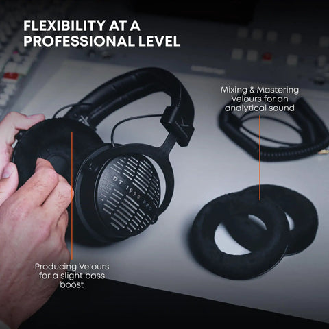 Hands holding DT 1990 Pro MKII Open-Back Wired Studio Headphones For Mixing And Mastering, 30 Ohm, with earpads on table.
