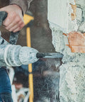 Side view of a rotary hammer drill drilling into a concrete wall with a carbide-tipped masonry bit
