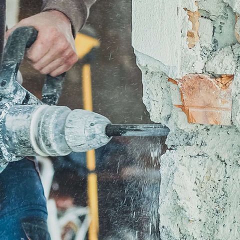 Side view of a rotary hammer drill drilling into a concrete wall with a carbide-tipped masonry bit