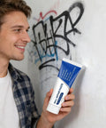 Man holding DIY Wall Repair Paste Kit 100g Waterproof Drywall Filler in front of graffiti wall, ready to use for repair.