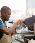 Barista using espresso machine in coffee shop with cups on the counter