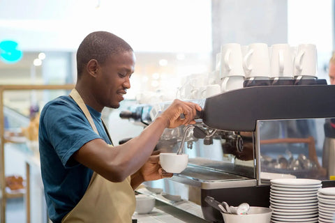 Barista using espresso machine in coffee shop with cups on the counter