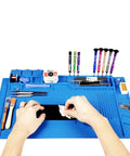 Heat Resistant Silicone Repair Mat With Built In Scale Ruler And Screw Positioning For Soldering Iron Phone And Computer Repair Size 17.7 By 11.8 Inches 124 Screw Holes 3 Covered Storage Pockets Keeps Workbench Safe From Heat, shown with tools and hands working on electronics.
