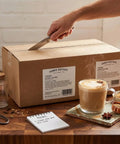 Person opening box of Creamy Instant Chai Latte Powder Mix For Hot Or Iced Drinks, Sweet Spiced Black Tea Latte with Milk and Honey