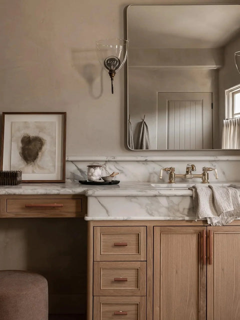 Bathroom vanity with marble countertop, featuring brown leather drawer pulls on wooden cabinets, large mirror above sink area.
