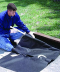 Worker installing Geotextile Drain Guard for 24-42 inch curb inlets, a heavy-duty oil and sediment shield, next to a catch basin.