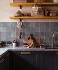 Kitchen with antique brass cabinet pulls on dark cabinets, featuring a tiled backsplash and wooden shelves with decorative items.
