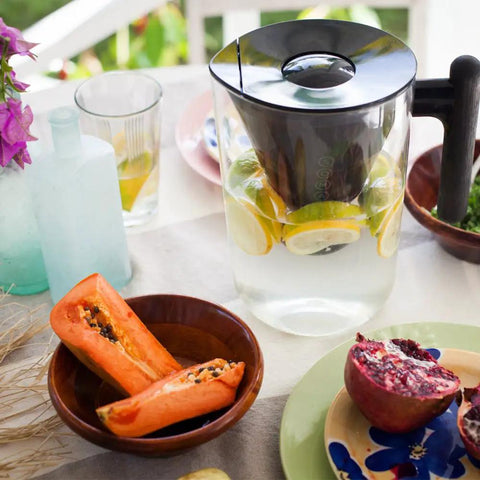 10 Cup Filtered Water Pitcher With Bamboo Handle, BPA Free Plastic, next to a fruit bowl, on a dining table outdoors