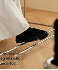 Footrest for leg relaxation underfoot, featuring a sturdy metal beam with a person's black loafers resting on it.