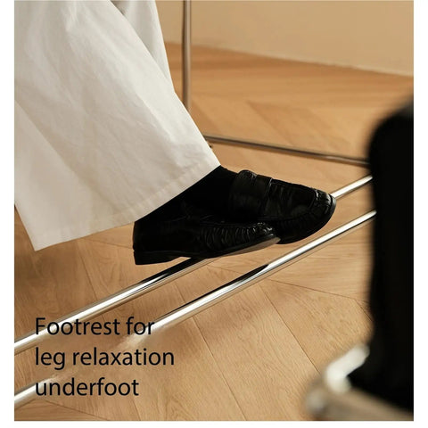 Footrest for leg relaxation underfoot, featuring a sturdy metal beam with a person's black loafers resting on it.