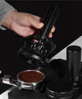 Hand holding a 58mm Electric Espresso Stirrer And Wdt Tool With Fine Needles over a portafilter filled with coffee grounds.