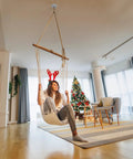 Woman sitting in a swing with Beast Mode Heavy Duty Two Pack Wall Mount Brackets For Suspension Straps Gym Rings And Body Weight Training With Industrial Steel Ceiling Anchors Supporting Up To Seven Hundred Fifty Pounds.
