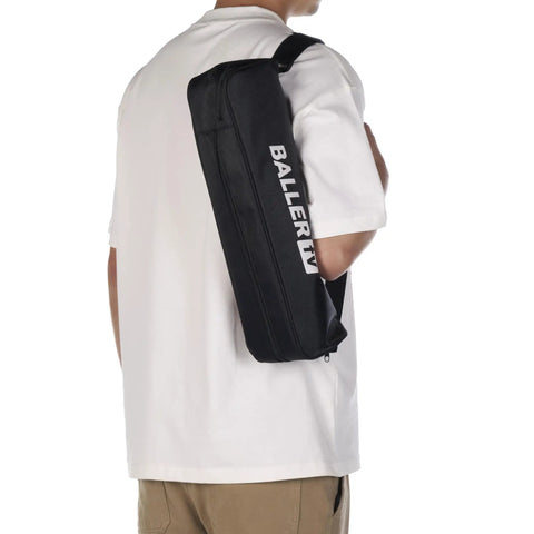 Person carrying black shoulder bag with 'BALLER' text, wearing a white shirt and khaki pants, view from the back.