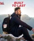 Man sitting on a rock with backpack holding Six Pack Emergency Mylar Blankets for Survival Gear and Outdoor Kits Space Blankets Reflective