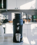 Game Changing Single Dose Coffee Grinder With 64 Millimeter Flat Burrs Stepless Adjustment Heavy Duty Zero Retention Build For Killer Espresso At Home Quiet Compact Design In Crisp White Finish on countertop.