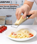 Person using Stainless Steel Handheld Cheese Grater With Soft Grip Handle And Zester over pasta, kitchen table background.