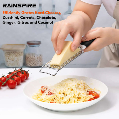 Person using Stainless Steel Handheld Cheese Grater With Soft Grip Handle And Zester over pasta, kitchen table background.