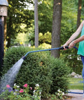Woman using Touch-N-Flow Rain Wand 16 Inch Length Green With One-Touch Lever for gentle full-flow watering of garden flowers.
