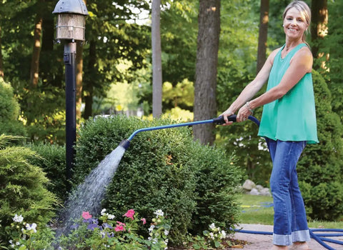 Woman using Touch-N-Flow Rain Wand 16 Inch Length Green With One-Touch Lever for gentle full-flow watering of garden flowers.