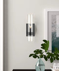 Modern Farmhouse Glass Cylinder Wall Sconce 1 Light Black Vanity Light Fixture on white wall with plant and artwork