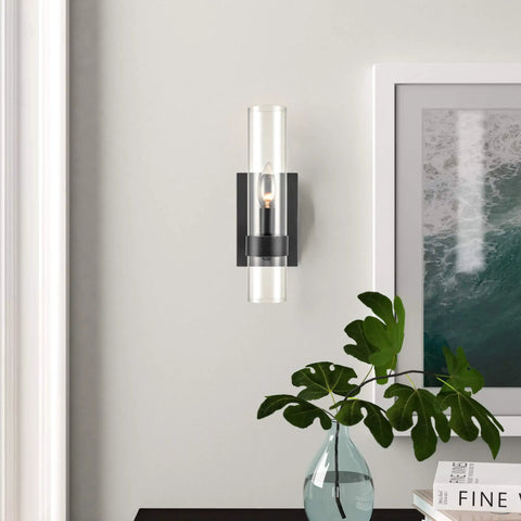 Modern Farmhouse Glass Cylinder Wall Sconce 1 Light Black Vanity Light Fixture on white wall with plant and artwork