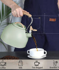 3 Liter Teapot With Loud Whistle Stainless Steel Stove Top Kettle With Wood Pattern Folding Handle Green Food Grade Teapot For Tea Lovers Coffee Buffs And Milk On The Stove Perfect For Daily Tea Or Coffee Rituals shown pouring liquid into cup held by person in apron.
