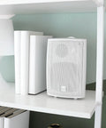 White Five Point Twenty Five Inch Three Way Outdoor Indoor Wired Speakers With Weather Resistant Build on a shelf indoors