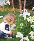 Child smelling a flower with whimsical balloon animals, showcasing 100 Pcs Clear Long Latex Model Balloons No Fuss Twisting Surface Prime Grade Heavy Duty Rubber For Kids Party Carnival Decor And Big Time Sculpture Art Projects.