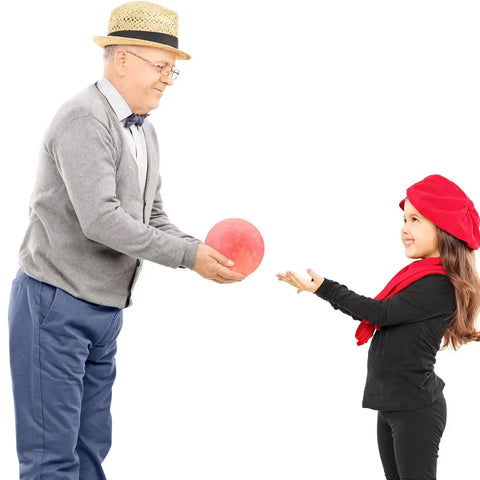 Older man in a hat handing a red ball to a young girl in a red beret, both smiling