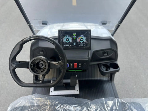 Interior view of White Eight Passenger Electric Golf Cart Rolled Up Tight With Beefy Dual Arm Suspensions Silky Smooth Five Kilowatt Motor Plus Touchscreen Audio And Deep Reclining Lounge Seats showing steering wheel and dashboard.