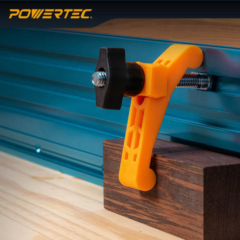 Two Pack Mini Hold Down Clamps For T Track Systems Three And A Quarter Inch Long By Three Quarters Inch Wide Includes Two And A Half Inch T Track Bolts Thumb Knobs And Swivels Ideal For CNC Machines Table Saw Sleds Drill Presses And Workbenches, installed on a blue T-track, clamping a wooden piece with an orange plastic body and black knob.