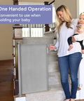Woman holding a baby using retractable mesh baby gate for stairs and doorways, extra wide up to 71 inches, 33 inches tall, easy install