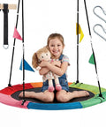 Child sitting on 40 Inch Saucer Tree Swing For Kids And Adults, Waterproof Heavy Duty Flying Swing, multicolored with hanging straps.