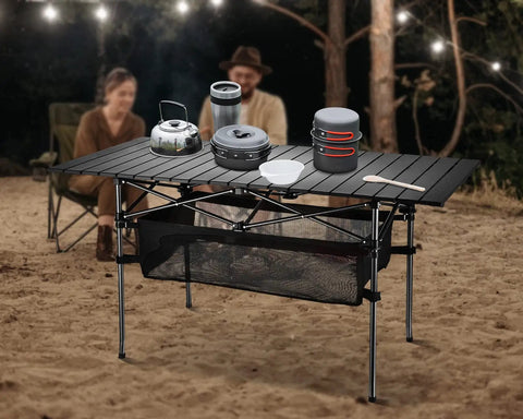 Lightweight Aluminum Folding Camping Table With Portable Roll Up Design For Outdoor Dining On The Go No Fuss Easy Setup 47 Inch By 22 Inch By 27 Inch Waterproof With Carrying Bag For Camping Beach Patio Picnic showcasing durability and versatility in a beach setting with cooking utensils.