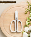 Ultra Sharp Garden Shears For Plants And Bonsai Pruning Stainless Steel With Anti Slip Serrations Effortless Cutting Through Half Inch Branches Clean Smooth Cuts For Floral Arranging And Garden Care On The Go on a wooden board next to white flowers
